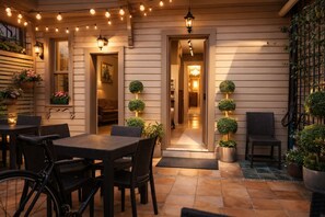 Une terrasse extérieure aménagée avec des meubles en osier, des plantes en pot et des guirlandes lumineuses.