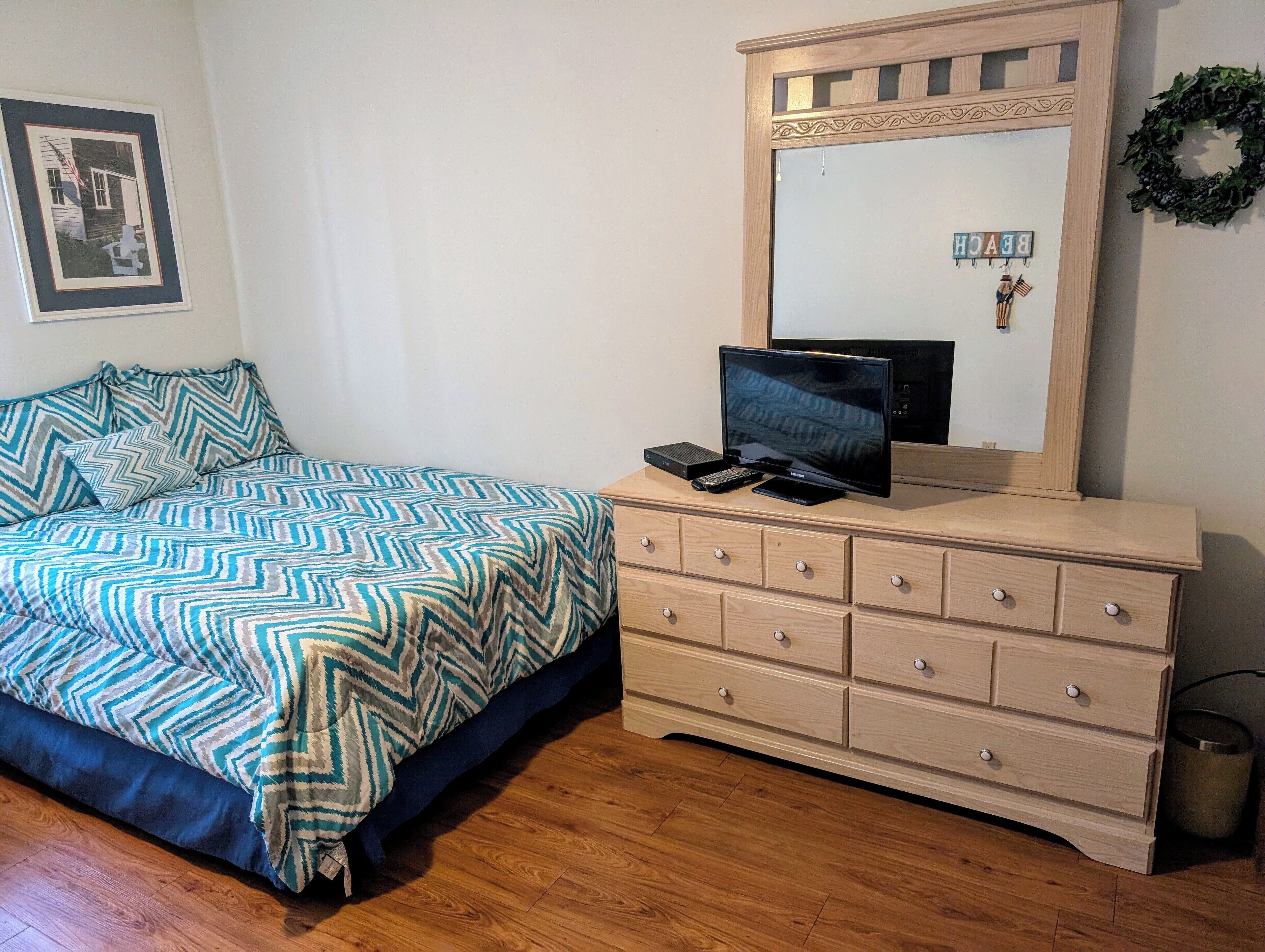 A bedroom with a bed, a dresser, a television, and a mirror.