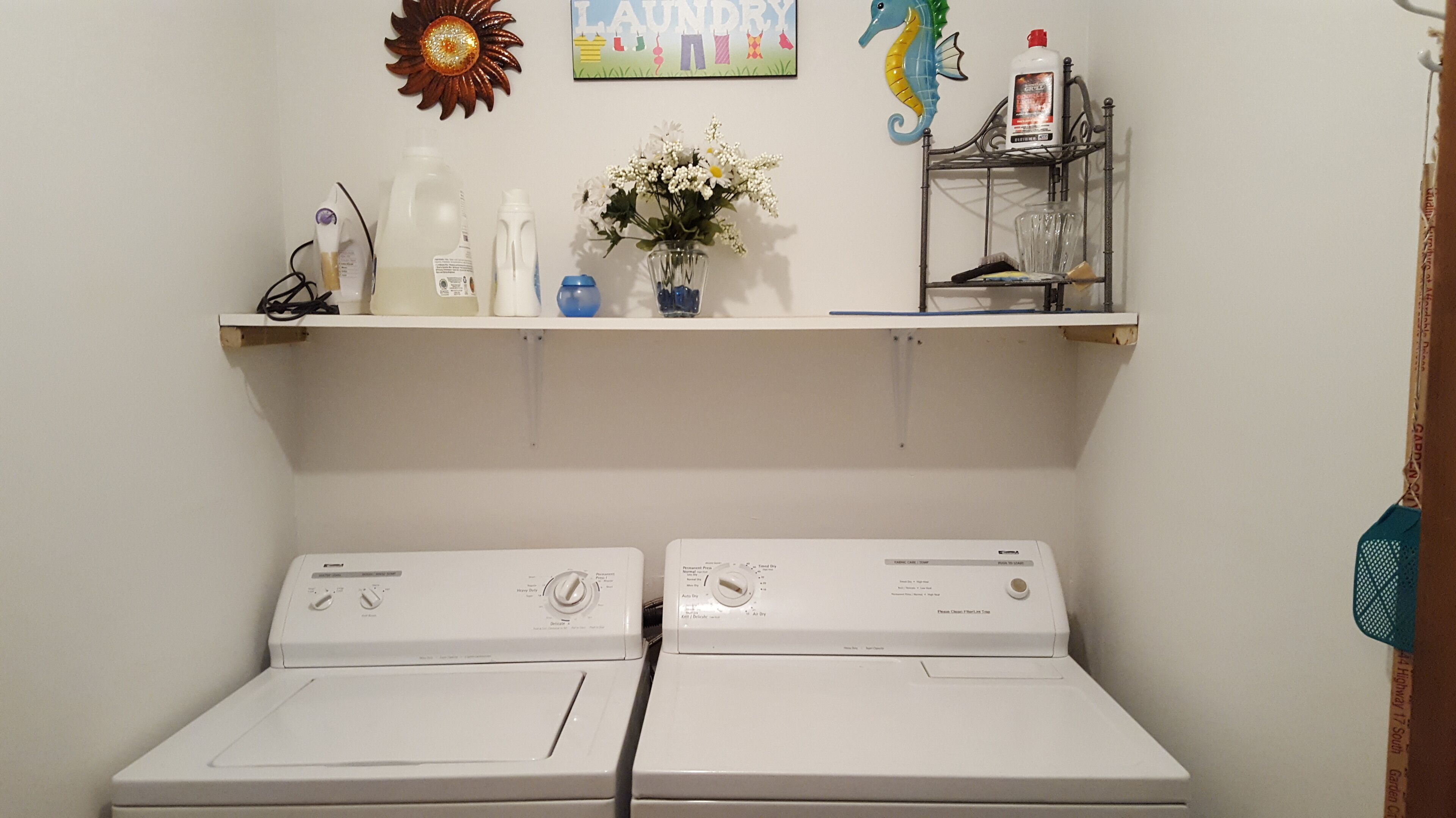 A laundry area with two front-loading washing machines, a shelf with various items, and a decorative wall piece.