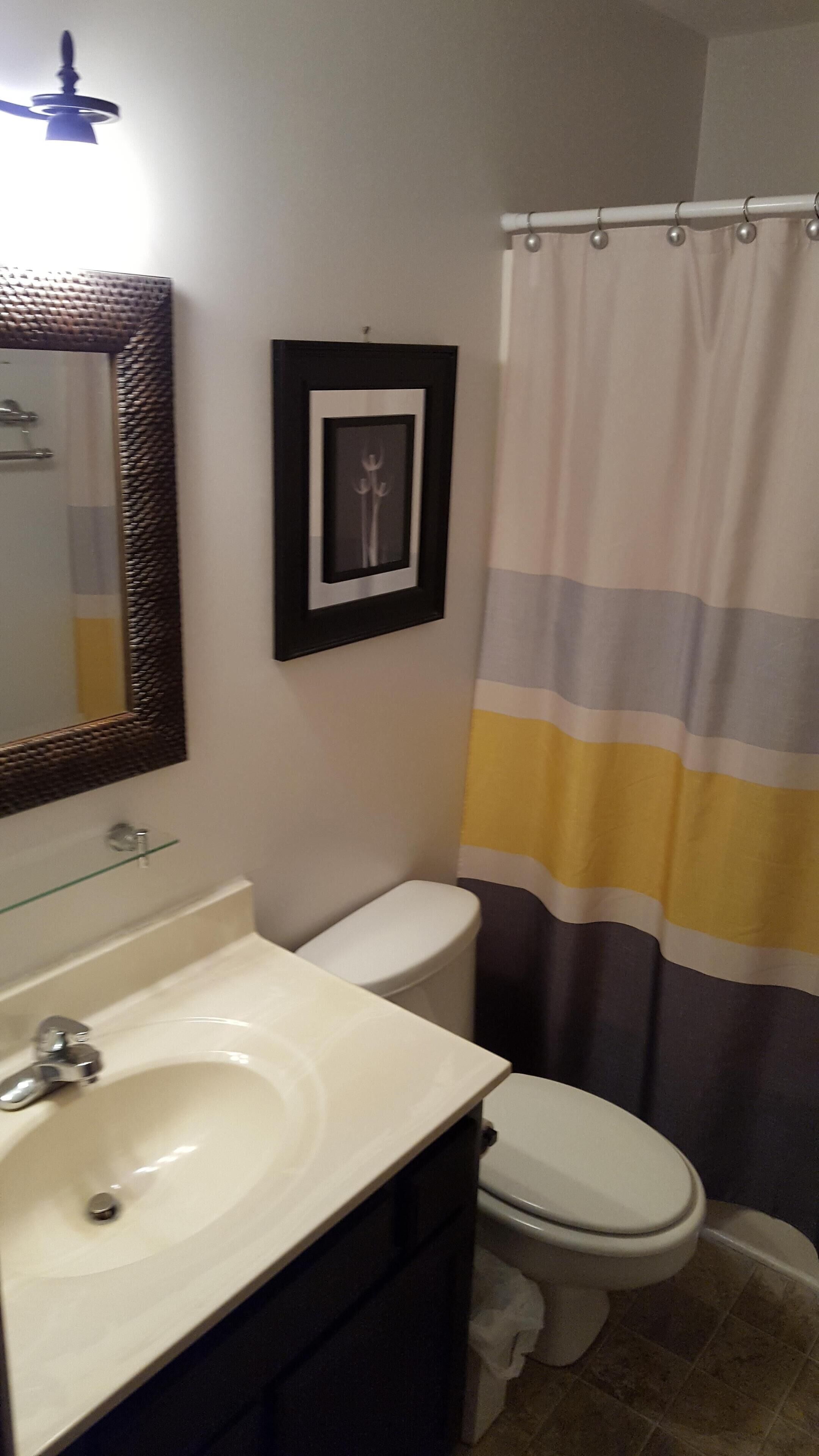 A bathroom with a white sink, a framed picture on the wall, a toilet, and a striped shower curtain.