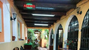 A corridor with wooden benches, potted plants, and a sign reading "AMERITO". - Hotel Internacional Guest House (Antigua Guatemala)