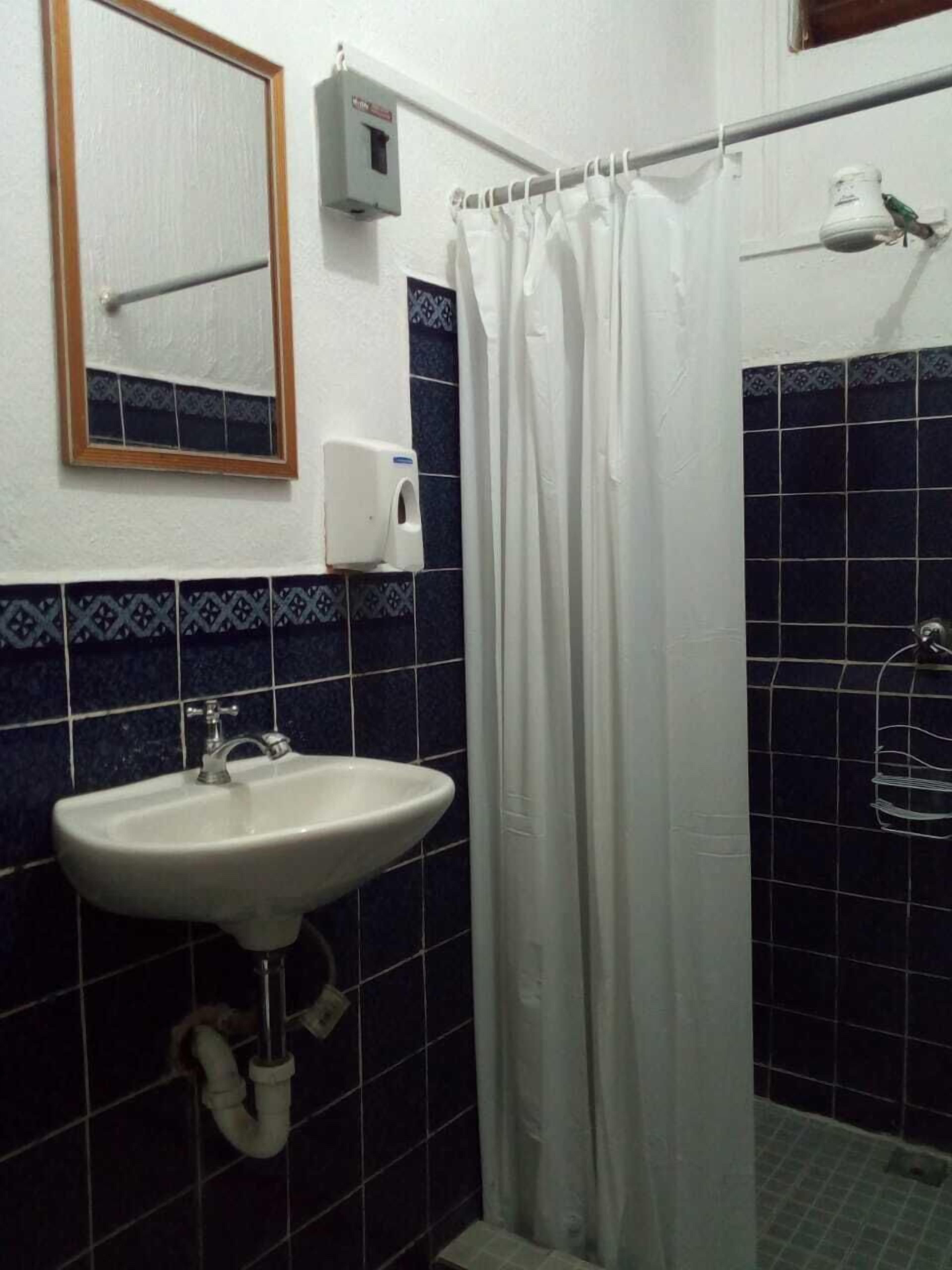 Une salle de bain avec un lavabo blanc, un miroir, un rideau de douche et un sèche-mains.