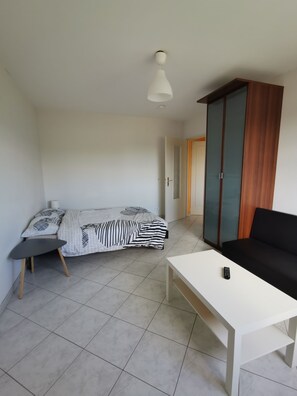A bedroom with a bed, a white table, a black sofa, and a wardrobe. - Charming 1 room, kitchen, bathroom of 35 m2 in very quiet residence. (Mulhouse)
