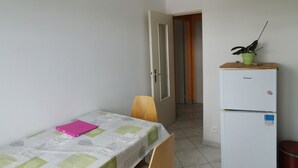 Una stanza piccola e pulita con un tavolo da pranzo, sedie, una lampada a soffitto bianca, un frigorifero e una porta che conduce a un'altra stanza.