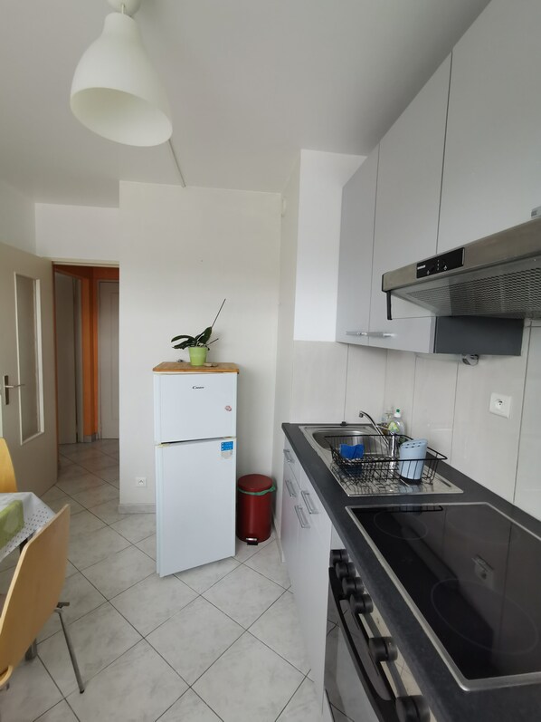 A modern kitchen with white cabinets, a black stove, and a small sink. - Charming 1 room, kitchen, bathroom of 35 m2 in very quiet residence. (Mulhouse)
