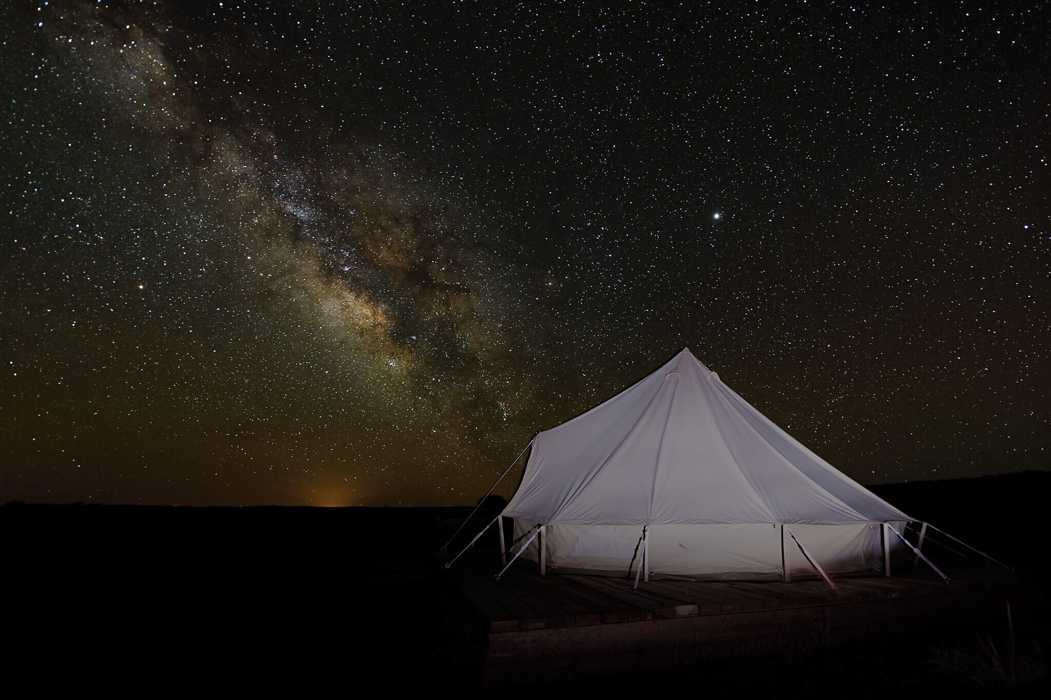 A white tent under a starry night sky with the Milky Way visible.