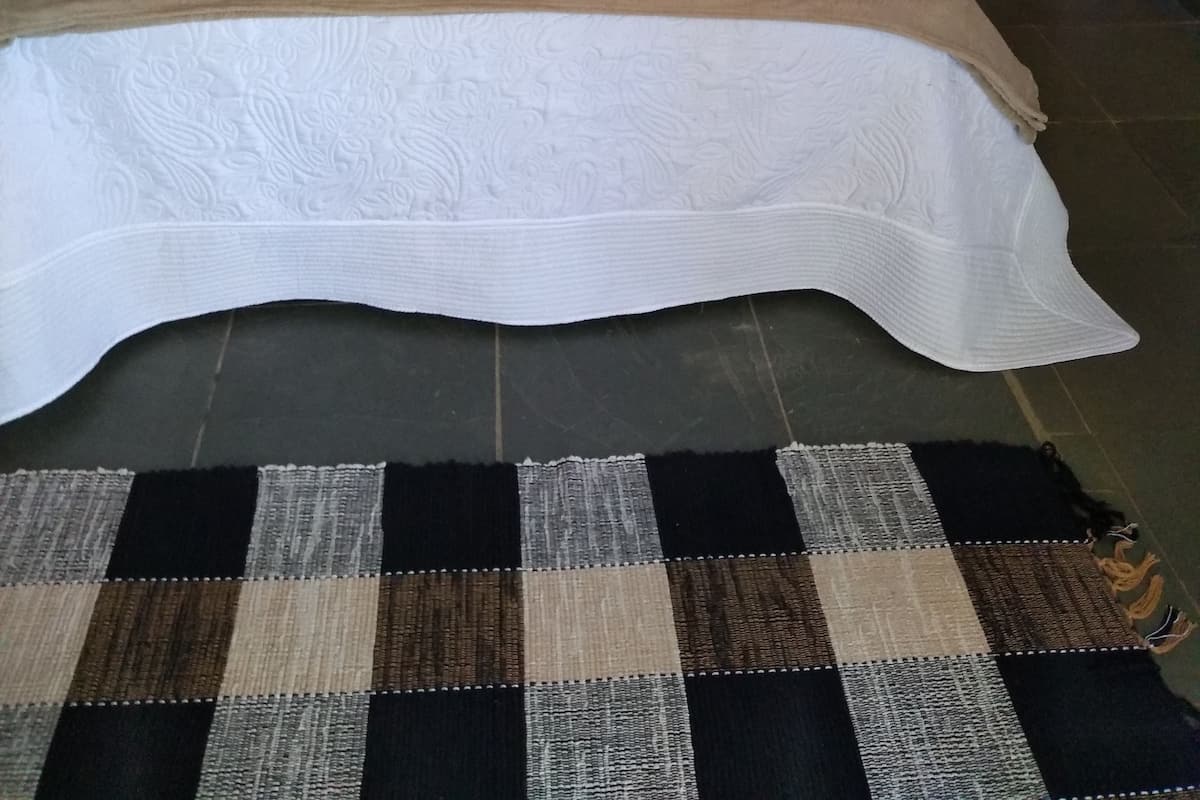 Cama bem arrumada com almofadas estampadas e tapete xadrez em quarto de hotel.