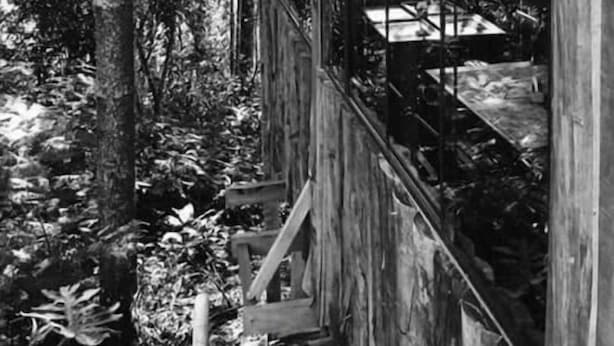 Una baita di legno con ampie finestre, immersa tra gli alberi.