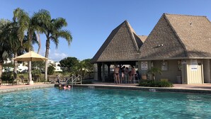 Ein Pool mit klarem Wasser, umgeben von Palmen und einem Gebäude mit einem Kachel­dach.