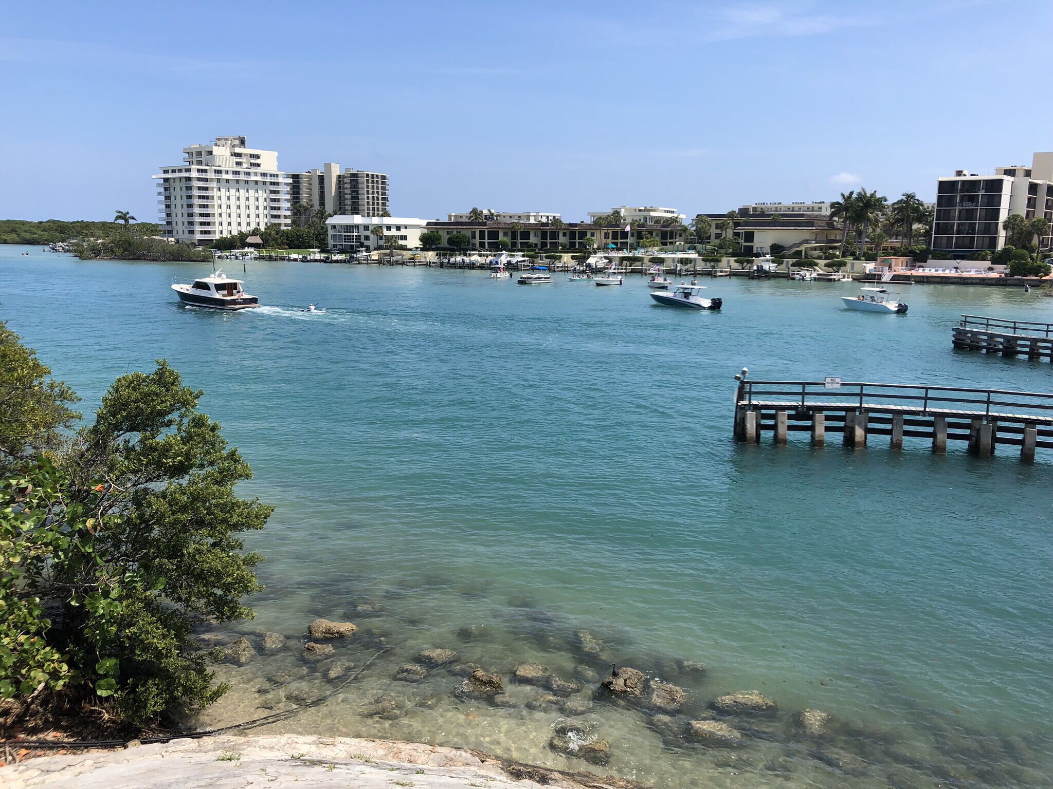 A marina with several boats docked, clear water, and buildings in the background.