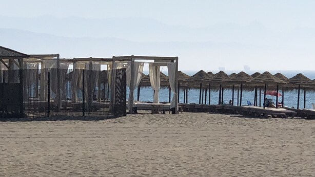 Ein Strand mit strohgedeckten Gebäuden und einem sandigen Vordergrund.