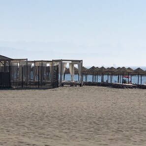 En strand med byggnader som har tak av halmtak och en sandstrand i förgrunden.