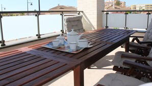 Ein Holztisch mit einer Tablett voller weißer Teekannen und Tassen, ein gepolsterter Stuhl und im Hintergrund ein Blick auf Gebäude.