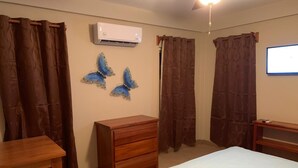 A bedroom with a bed, a wooden dresser, a desk, and a wall-mounted air conditioner. - Mid Town Loaf rental (San Pedro)