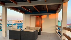 A covered outdoor seating area with wicker furniture and a wooden door. - Mid Town Loaf rental (San Pedro)