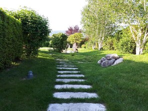 A stone pathway leading through a well-maintained garden with lush greenery and a variety of trees.