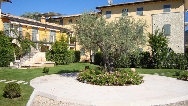 A courtyard with a central tree, surrounded by a circular stone pathway, and adjacent buildings with balconies and a staircase. - Prestigious penthouse with large panoramic terrace (Marciaga)