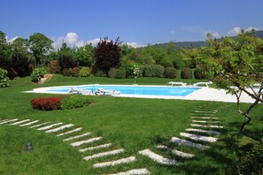 Uma piscina com espreguiçadeiras e um caminho de pedra que a leva, cercada por vegetação exuberante e árvores.