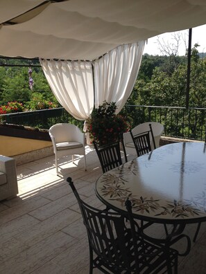 Pátio externo com mesa redonda e quatro cadeiras, rodeado por um toldo branco.