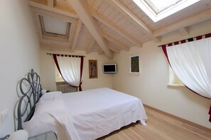 Quarto com cama, televisão, janela com cortinas e claraboia.