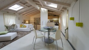 A spacious living room with a glass-top dining table, white sofas, and a kitchen in the background. - Prestigious penthouse with large panoramic terrace (Marciaga)