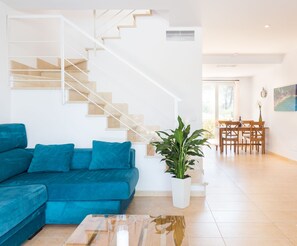 Een moderne woonkamer met een blauwe modulaire bank, een houten trap en een eethoek met houten meubels.