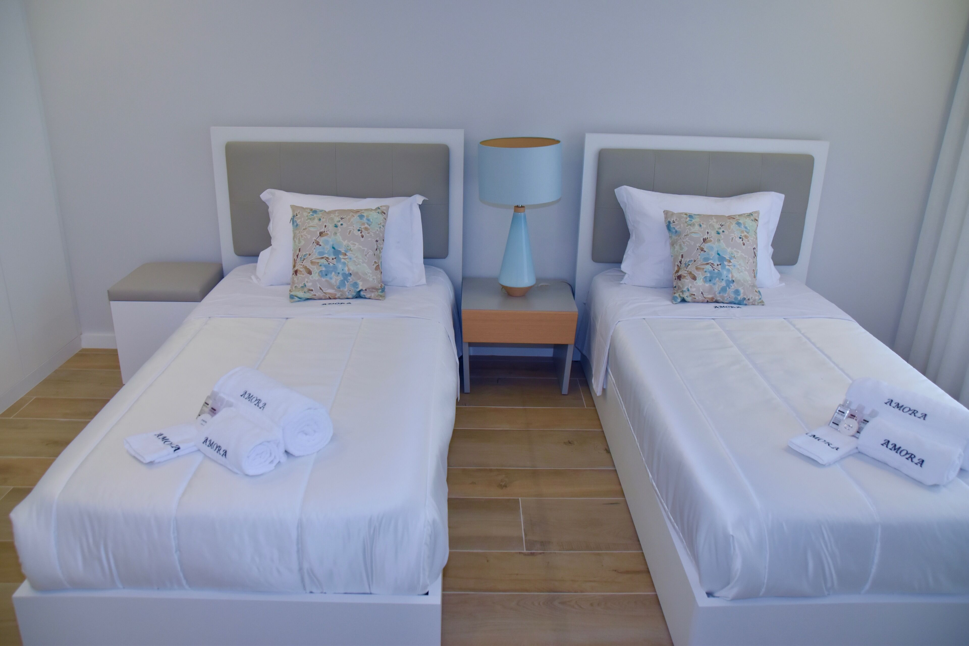 A hotel room with two beds, each with a pillow and a lamp between them. There are towels on the beds and a nightstand with a lamp.