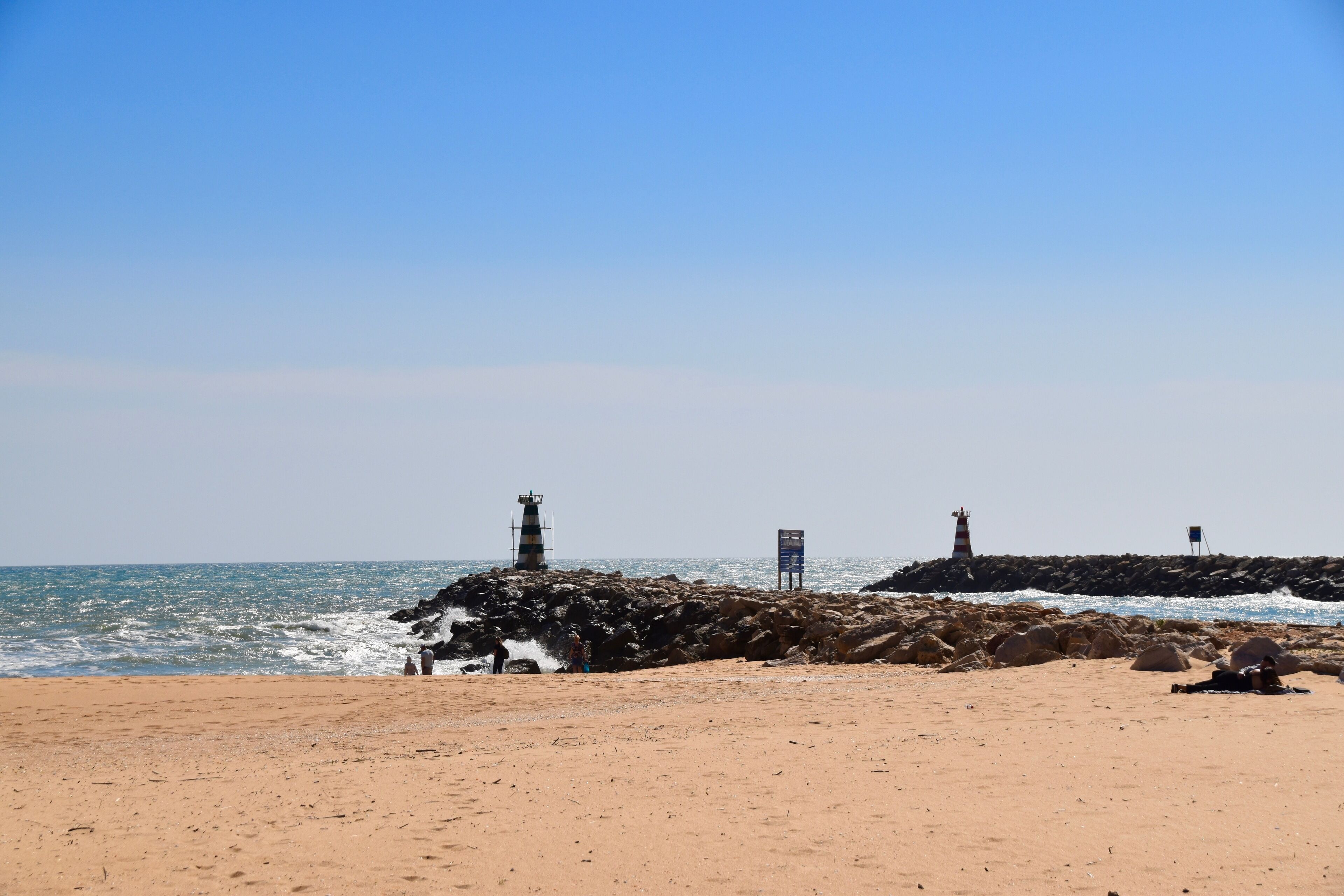 Une plage parsemée de rochers, avec deux phares visibles à l’arrière-plan.