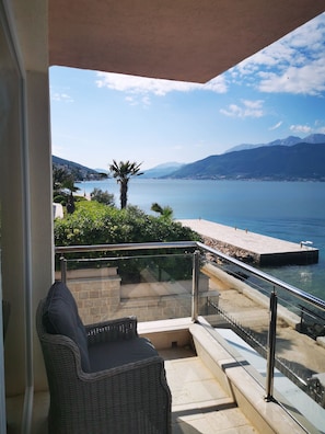 A balcony with wicker furniture, a stone wall, and a view of a lake and mountains. - Waterline property with breathtaking views and pool (Krašići)