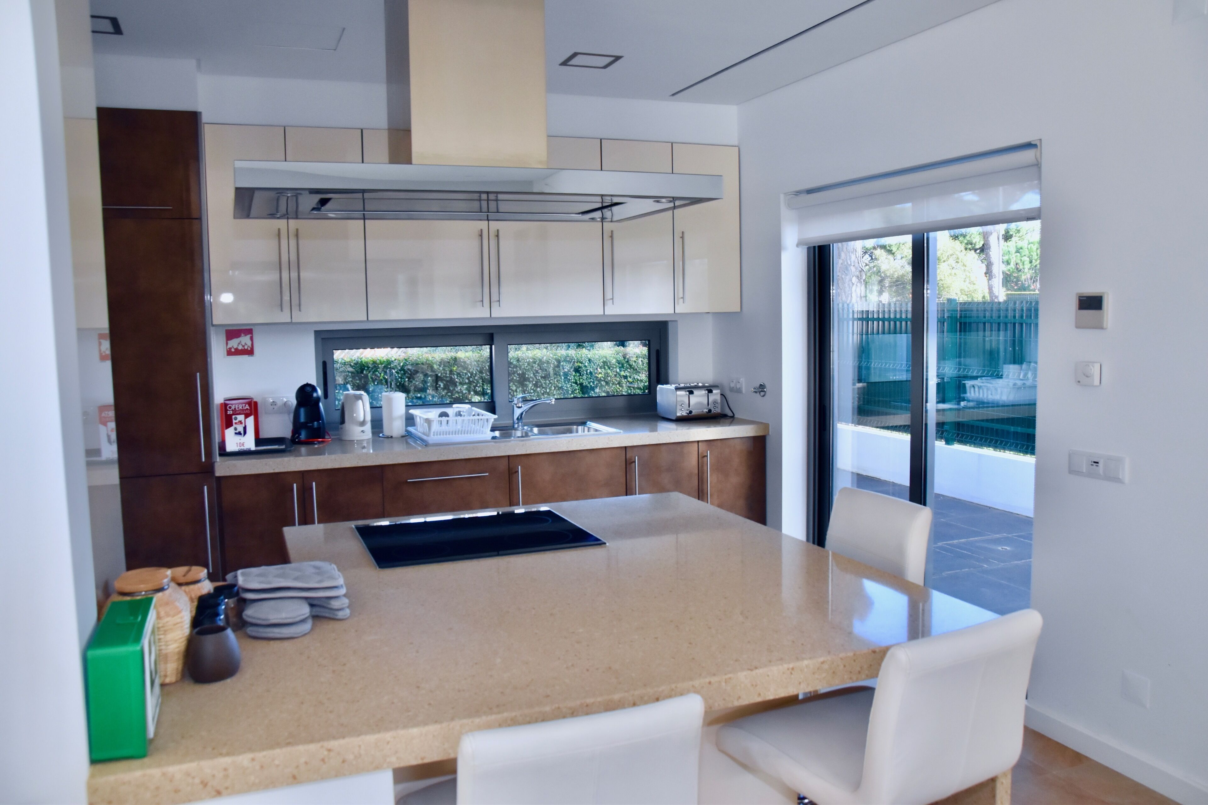 Een moderne keuken met een groot eiland, inbouwmeubels en uitzicht op buiten.