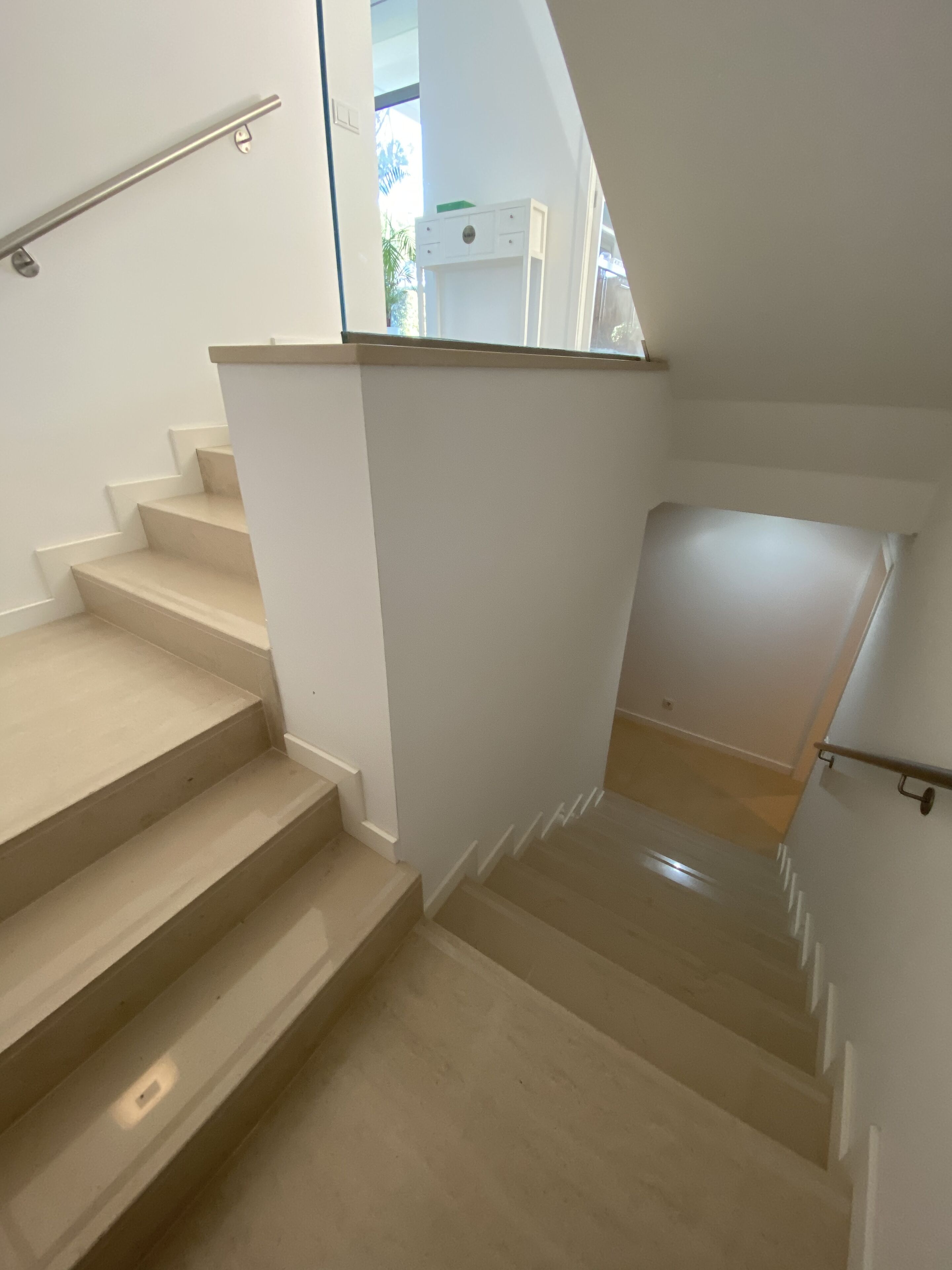 A staircase with beige steps and white walls, leading to a landing with a glass door.