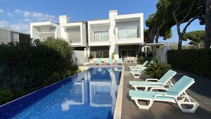 A modern hotel with a swimming pool, lounge chairs, and a clear blue sky. - Amora Villa-Vilamoura (vilamoura)