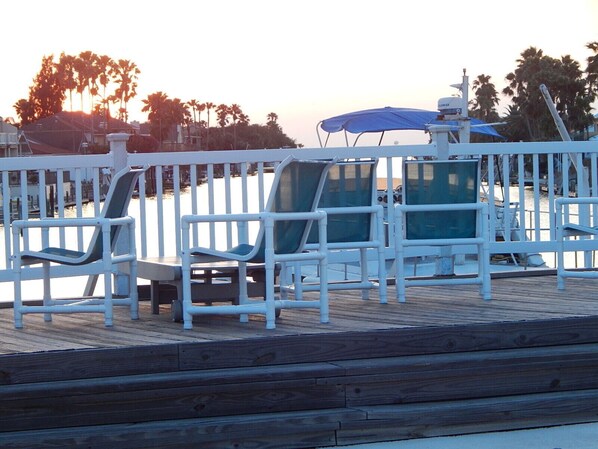 A wooden deck with white railings, two blue umbrellas, and a boat in the background.