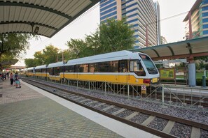 Un treno in una stazione con banchina coperta, binari e moderni edifici sullo sfondo.