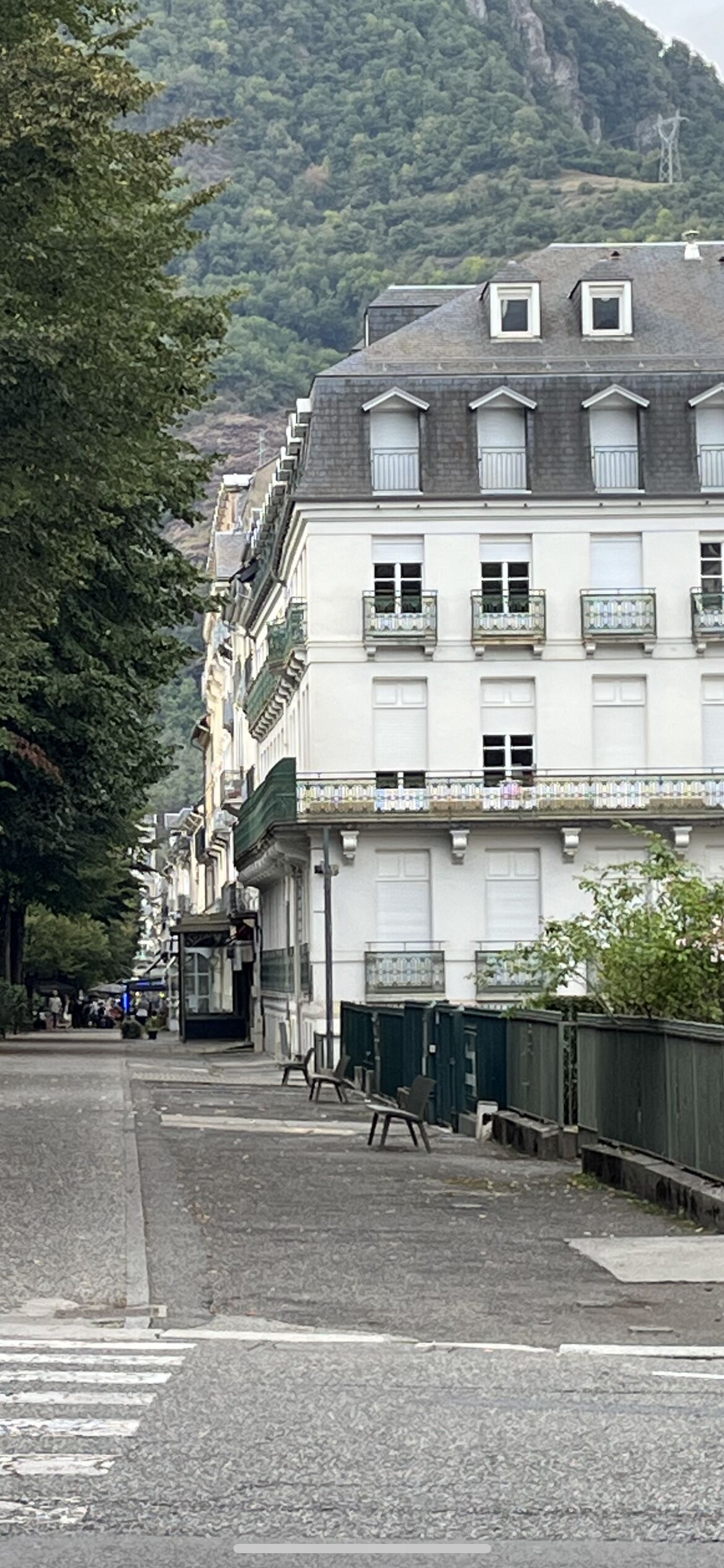 Une rangée de bâtiments blancs dotés de balcons, un passage piéton et une montagne en arrière-plan.