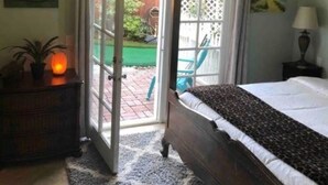 Quarto com cama, ventilador de teto, mesa de cabeceira, abajur e vista para o exterior por uma porta de correr de vidro.