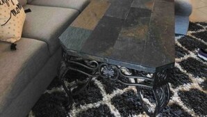Uma sala de estar com sofá seccional, mesa de centro escura e tapete estampado.