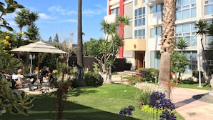 A courtyard with outdoor seating, palm trees, and a modern building with a red accent. - Dali Suites – Accommodations in Playas de Tijuana (Tijuana)