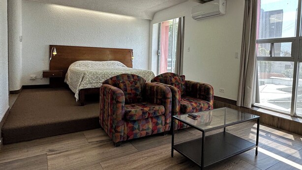 A hotel room with a bed, a sofa, a coffee table, and large windows. - Dali Suites – Accommodations in Playas de Tijuana (Tijuana)
