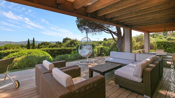 An outdoor patio with wicker furniture, a hanging chair, and a view of the landscape. - Near the beach, villa 8 persons with a pool and air-conditioned bedrooms. (GRIMAUD)