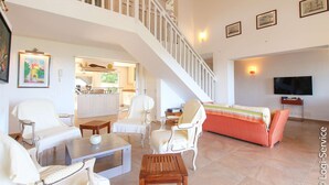 A spacious living area with a staircase, white furniture, a kitchen in the background, and a TV on the wall. - Near the beach, villa 8 persons with a pool and air-conditioned bedrooms. (GRIMAUD)