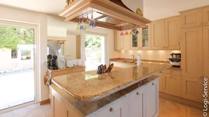 A modern kitchen with a granite countertop, wooden cabinets, and a built-in oven. - Near the beach, villa 8 persons with a pool and air-conditioned bedrooms. (GRIMAUD)