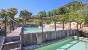 A wooden deck with a pool and lounge chairs, surrounded by greenery and hills. - Near the beach, villa 8 persons with a pool and air-conditioned bedrooms. (GRIMAUD)