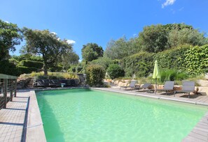 Una piscina cristalina con sillones de descanso y sombrillas, rodeada de vegetación y árboles.