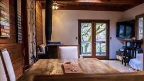 A cozy room with a wooden floor, a bed, a TV, and a sliding glass door leading to a balcony. - Gorgeous Secluded Treehouse with Spectacular Views (Carmel Valley)