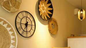 Una habitación con dos sillones de mimbre, un reloj de pared, decoración mural tejida, una lámpara colgante y una pequeña mesa con un cuenco.