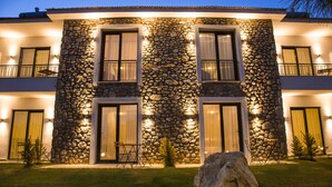 Un edificio de varios pisos con fachada de piedra, ventanas grandes y un balcón con barandilla.