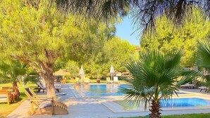 Un área de comedor al aire libre con piscina y sillones de descanso al fondo.