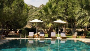Piscina con sillas de descanso y sombrillas, rodeada de árboles y un paisaje montañoso.