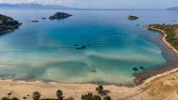 Un paisaje costero con agua cristalina, afloramientos rocosos y una playa de arena.